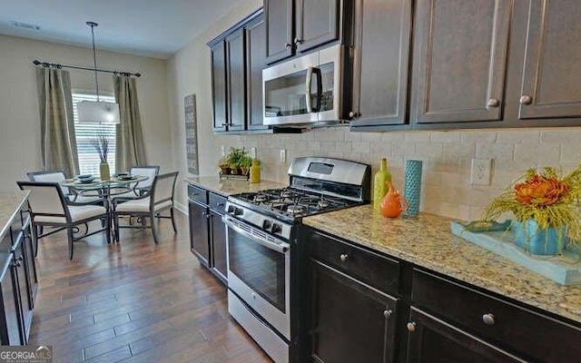 kitchen featuring decorative light fixtures, dark wood-type flooring, stainless steel appliances, light stone countertops, and dark brown cabinets