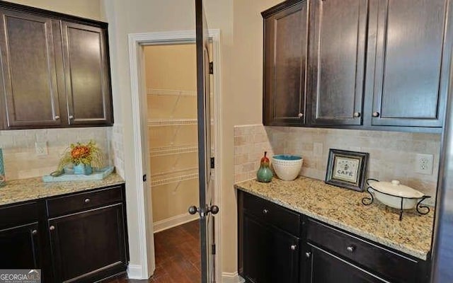 kitchen featuring dark wood-type flooring, light stone counters, backsplash, and dark brown cabinetry