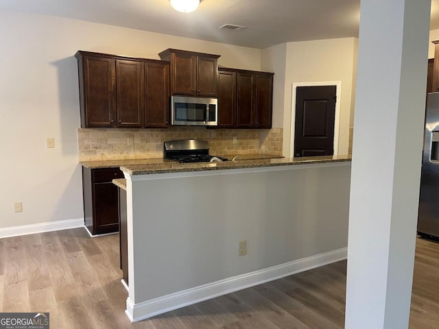 kitchen with dark brown cabinets, stainless steel appliances, light hardwood / wood-style floors, stone countertops, and kitchen peninsula