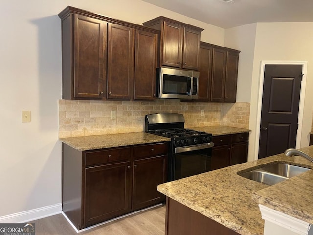 kitchen with black gas range oven, sink, dark brown cabinets, and light hardwood / wood-style floors