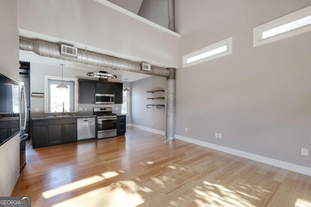 kitchen with sink, appliances with stainless steel finishes, hanging light fixtures, plenty of natural light, and a high ceiling