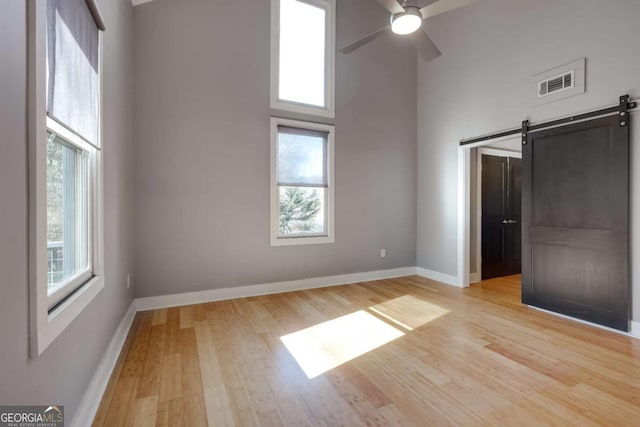 unfurnished bedroom featuring a barn door, a towering ceiling, ceiling fan, and light hardwood / wood-style flooring