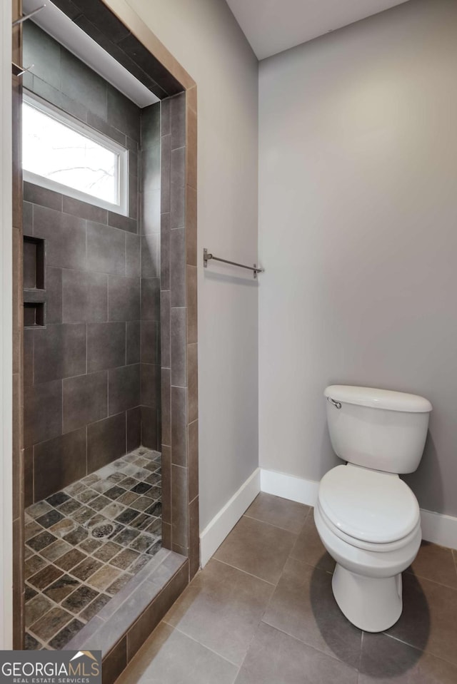 bathroom featuring toilet, tile patterned flooring, and a tile shower