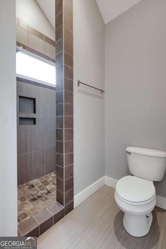 bathroom with a tile shower, vaulted ceiling, and toilet