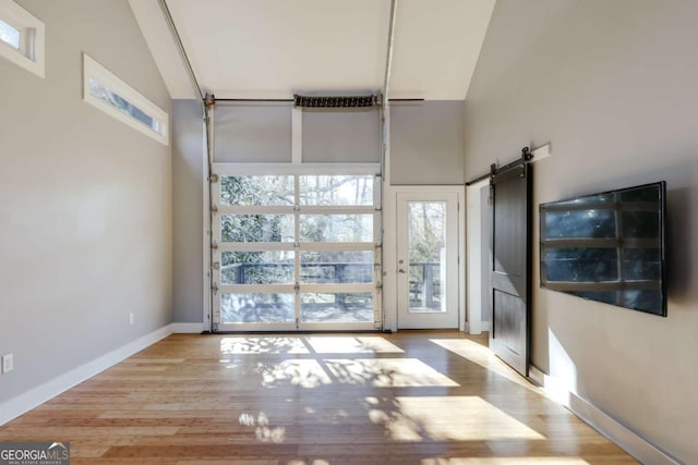 interior space with high vaulted ceiling, a barn door, and light hardwood / wood-style floors