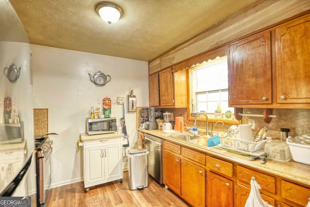 kitchen featuring sink, light hardwood / wood-style flooring, appliances with stainless steel finishes, a textured ceiling, and decorative backsplash