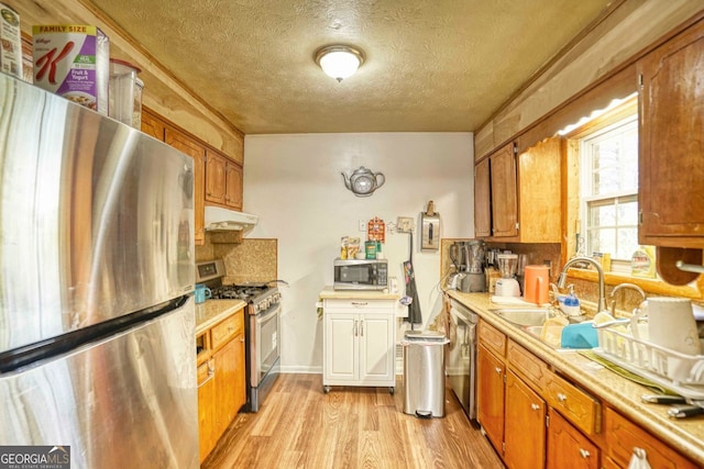 kitchen with appliances with stainless steel finishes, light hardwood / wood-style floors, sink, and a textured ceiling