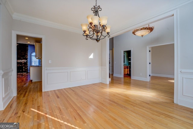 unfurnished room with an inviting chandelier, ornamental molding, and light wood-type flooring