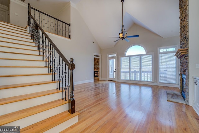 interior space featuring ceiling fan, a fireplace, a high ceiling, and light wood-type flooring