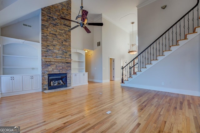 unfurnished living room featuring built in features, ceiling fan, a towering ceiling, a fireplace, and light hardwood / wood-style floors