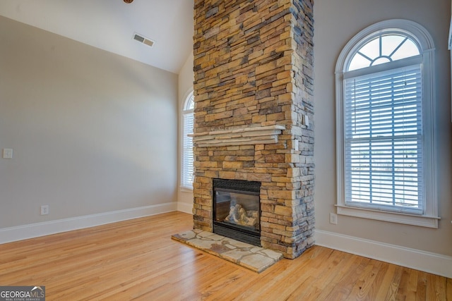 unfurnished living room with high vaulted ceiling, a fireplace, light wood-type flooring, and a wealth of natural light