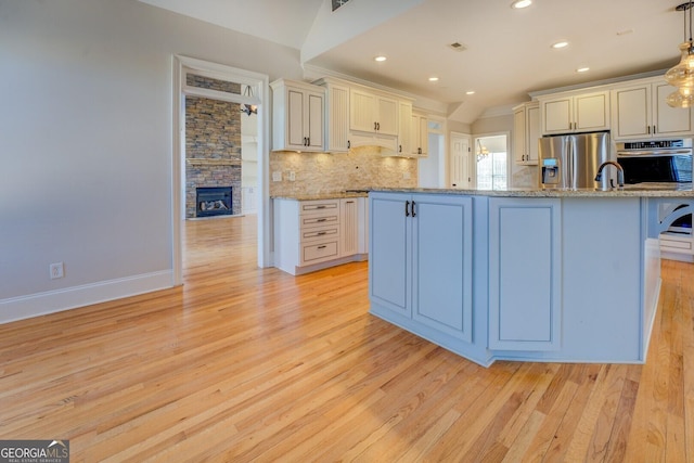 kitchen with stainless steel refrigerator with ice dispenser, light stone counters, a kitchen bar, decorative light fixtures, and light wood-type flooring