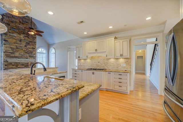 kitchen with stainless steel appliances, vaulted ceiling, light stone countertops, and cream cabinets