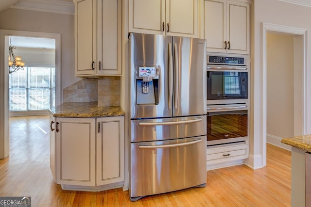 kitchen featuring stainless steel appliances, light stone counters, ornamental molding, decorative backsplash, and light wood-type flooring