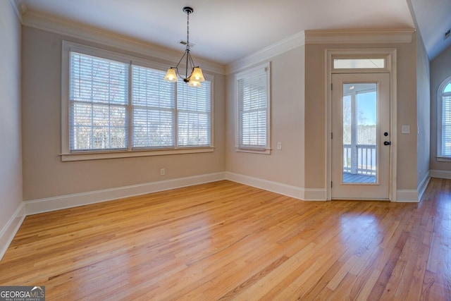 unfurnished dining area featuring a healthy amount of sunlight, ornamental molding, a chandelier, and light hardwood / wood-style flooring