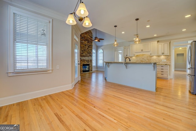 kitchen with light stone counters, light hardwood / wood-style flooring, stainless steel fridge, pendant lighting, and backsplash