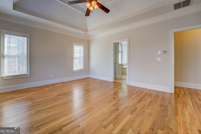 empty room featuring crown molding, a tray ceiling, light hardwood / wood-style floors, and a wealth of natural light