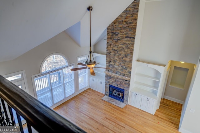 unfurnished living room featuring a stone fireplace, hardwood / wood-style floors, ceiling fan, and built in shelves