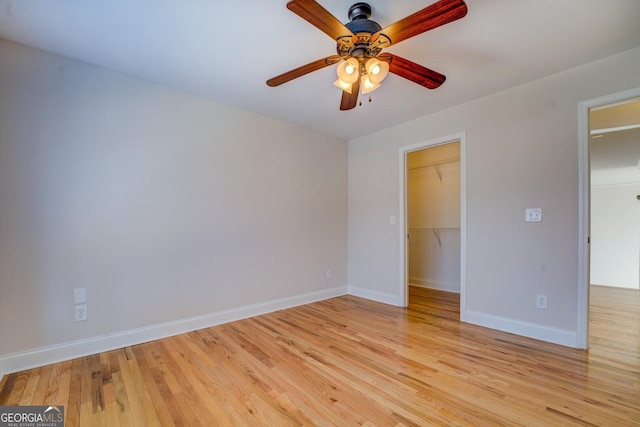 unfurnished bedroom with ceiling fan, a spacious closet, a closet, and light wood-type flooring