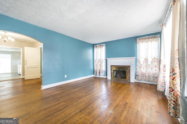 unfurnished living room featuring an inviting chandelier, dark hardwood / wood-style floors, a brick fireplace, and a textured ceiling