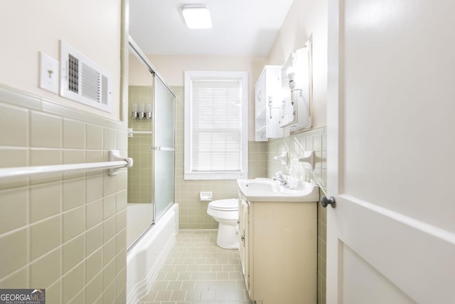 full bathroom with combined bath / shower with glass door, tile walls, tile patterned flooring, vanity, and toilet