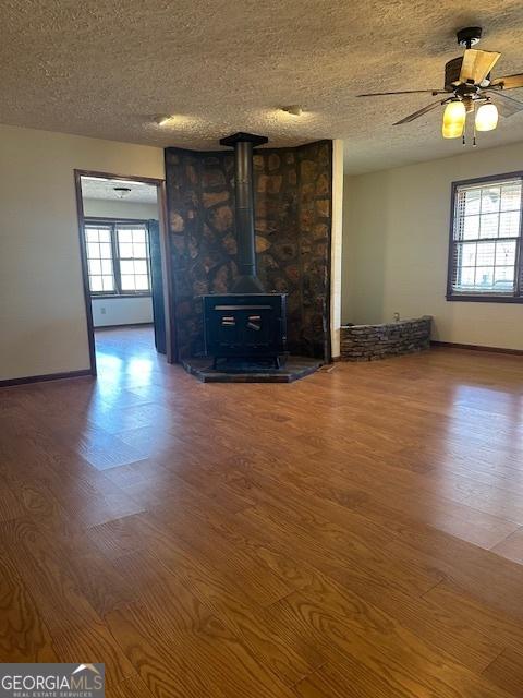 unfurnished living room featuring ceiling fan, wood-type flooring, a textured ceiling, and a wood stove