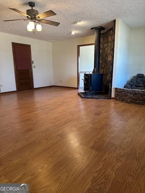 unfurnished living room featuring ceiling fan, a wood stove, hardwood / wood-style floors, and a textured ceiling