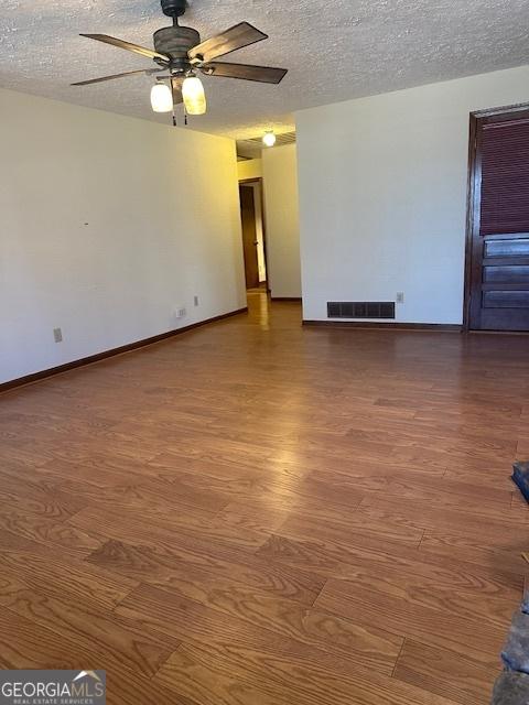 empty room with wood finished floors, visible vents, a textured ceiling, and ceiling fan
