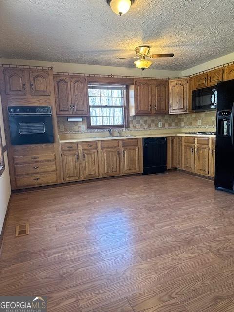 kitchen featuring light countertops, black appliances, and wood finished floors