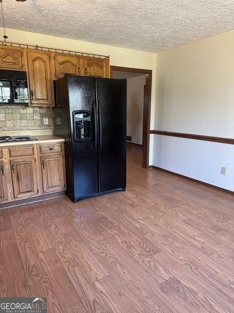 kitchen featuring light countertops, wood finished floors, backsplash, black appliances, and brown cabinets