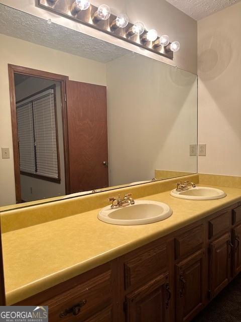 bathroom with double vanity, a textured ceiling, and a sink