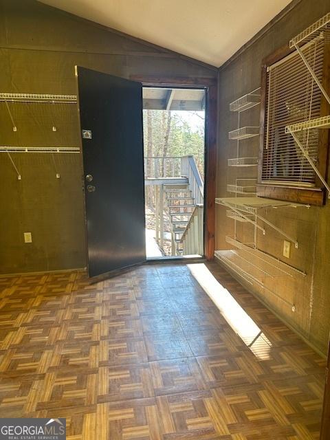 interior space with vaulted ceiling, dark parquet floors, and wood walls