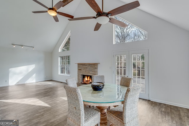 dining room with hardwood / wood-style floors, a fireplace, high vaulted ceiling, ceiling fan, and french doors