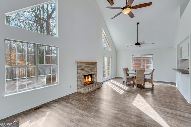 dining area featuring ceiling fan, a stone fireplace, high vaulted ceiling, and light hardwood / wood-style flooring