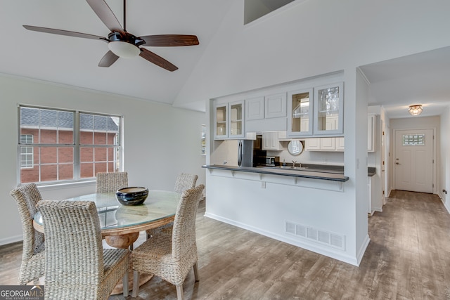 dining space with ceiling fan, high vaulted ceiling, sink, and hardwood / wood-style floors