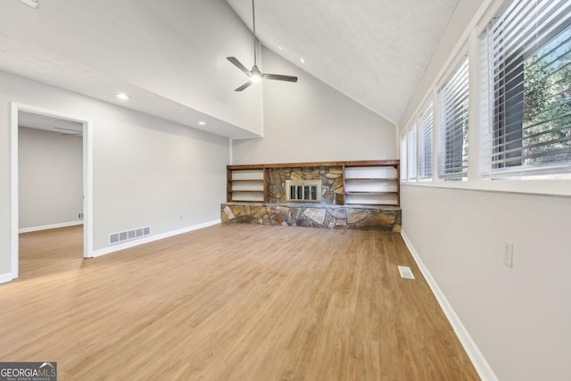 unfurnished living room featuring a stone fireplace, high vaulted ceiling, ceiling fan, and light wood-type flooring