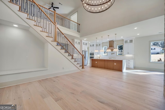 unfurnished living room with sink, ceiling fan with notable chandelier, light hardwood / wood-style flooring, and a high ceiling