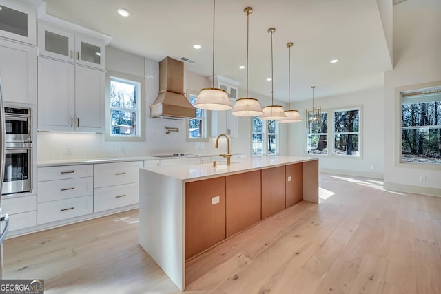 kitchen featuring white cabinetry, backsplash, a kitchen island with sink, and premium range hood