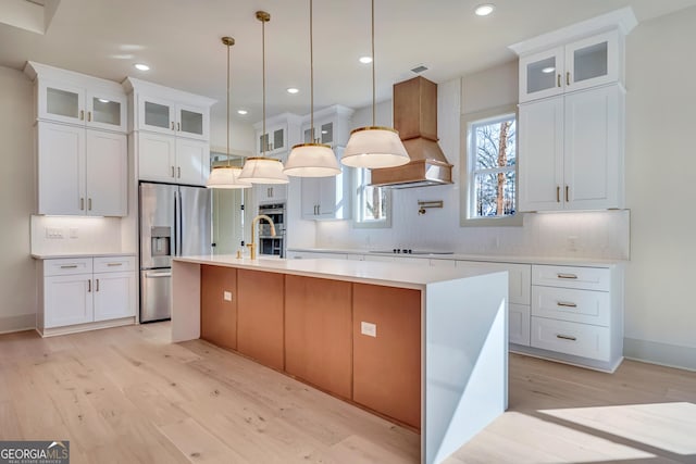 kitchen featuring white cabinetry, appliances with stainless steel finishes, premium range hood, and a center island with sink