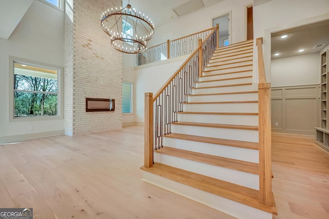 stairs with hardwood / wood-style flooring, a brick fireplace, a towering ceiling, and a notable chandelier