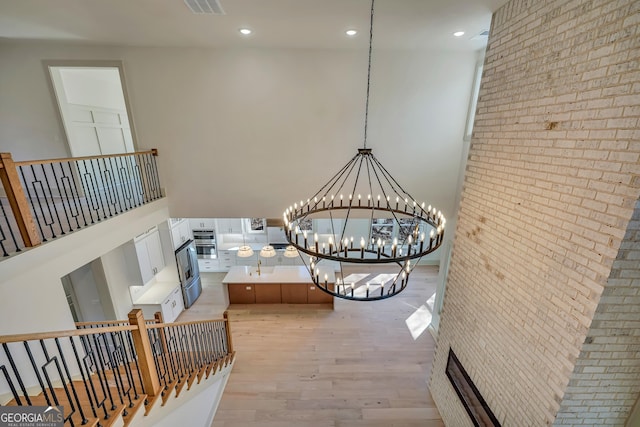 interior space with a towering ceiling, brick wall, light hardwood / wood-style floors, and a notable chandelier