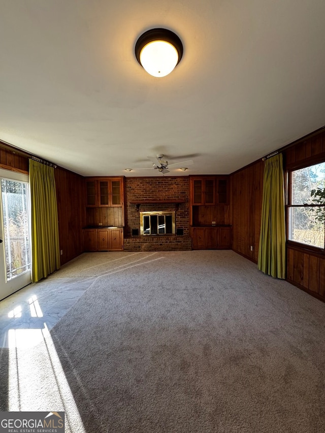 unfurnished living room featuring ceiling fan, light colored carpet, a brick fireplace, and wood walls