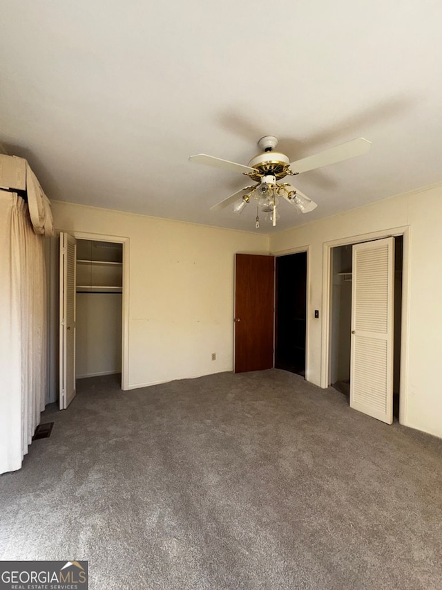 unfurnished bedroom featuring dark colored carpet, two closets, and ceiling fan