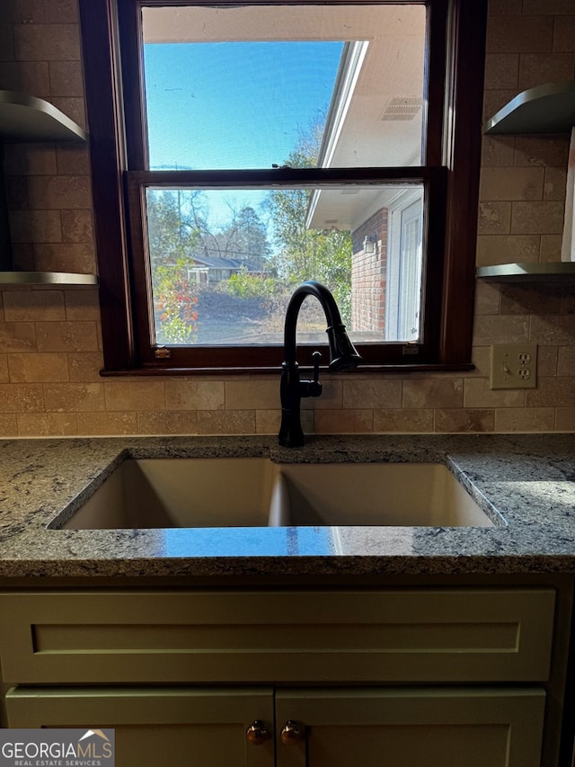 interior details featuring tasteful backsplash, light stone countertops, sink, and cream cabinetry