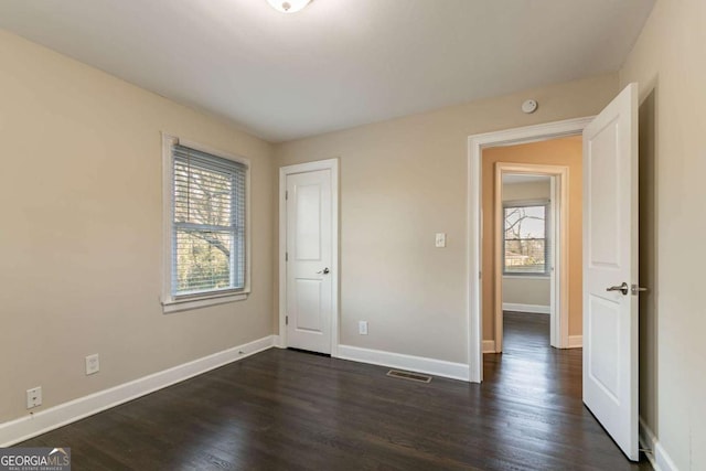 unfurnished bedroom featuring multiple windows and dark hardwood / wood-style flooring