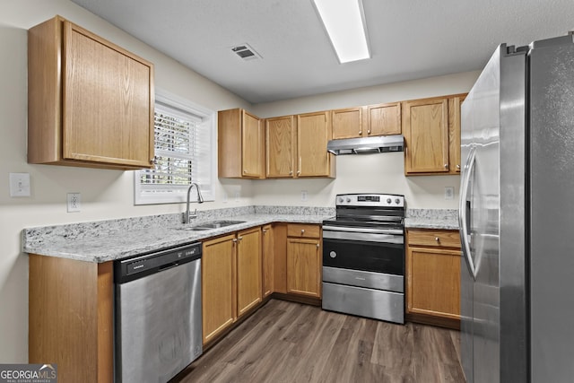 kitchen with appliances with stainless steel finishes, dark hardwood / wood-style floors, light stone countertops, and sink