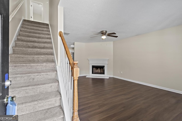 staircase with hardwood / wood-style floors, a textured ceiling, and ceiling fan