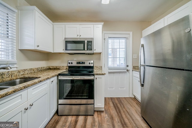 kitchen with sink, appliances with stainless steel finishes, hardwood / wood-style floors, light stone counters, and white cabinets