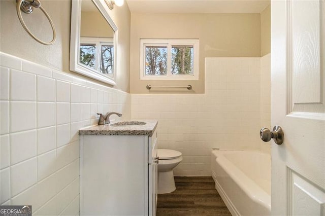 bathroom featuring a washtub, tile walls, hardwood / wood-style floors, vanity, and toilet