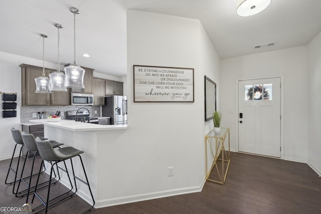 kitchen featuring dark wood finished floors, light countertops, appliances with stainless steel finishes, tasteful backsplash, and a kitchen bar